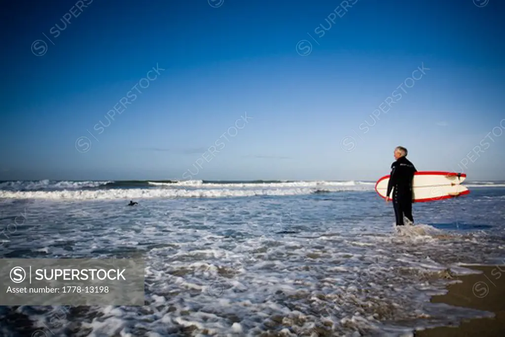 A surfer stands at the waters edge and prepares for a session in Carlsbad, CA