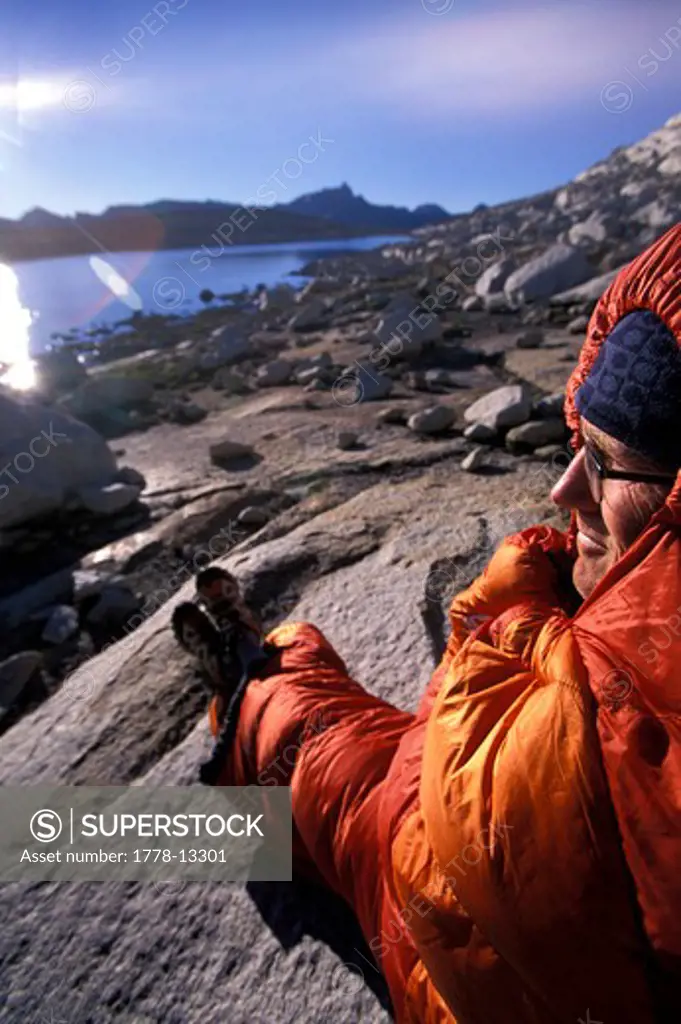 A bacpacker enjoying the morning in his sleeping bag and looking out over a mountain lake on the Sierra High Route