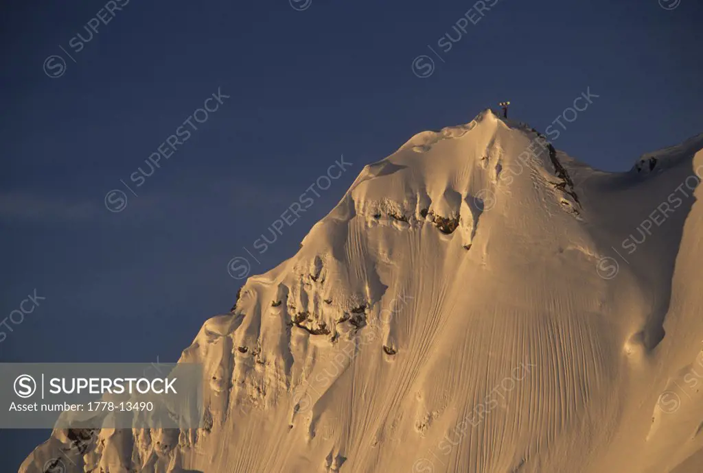 A man standing on a mountain peak at sunset