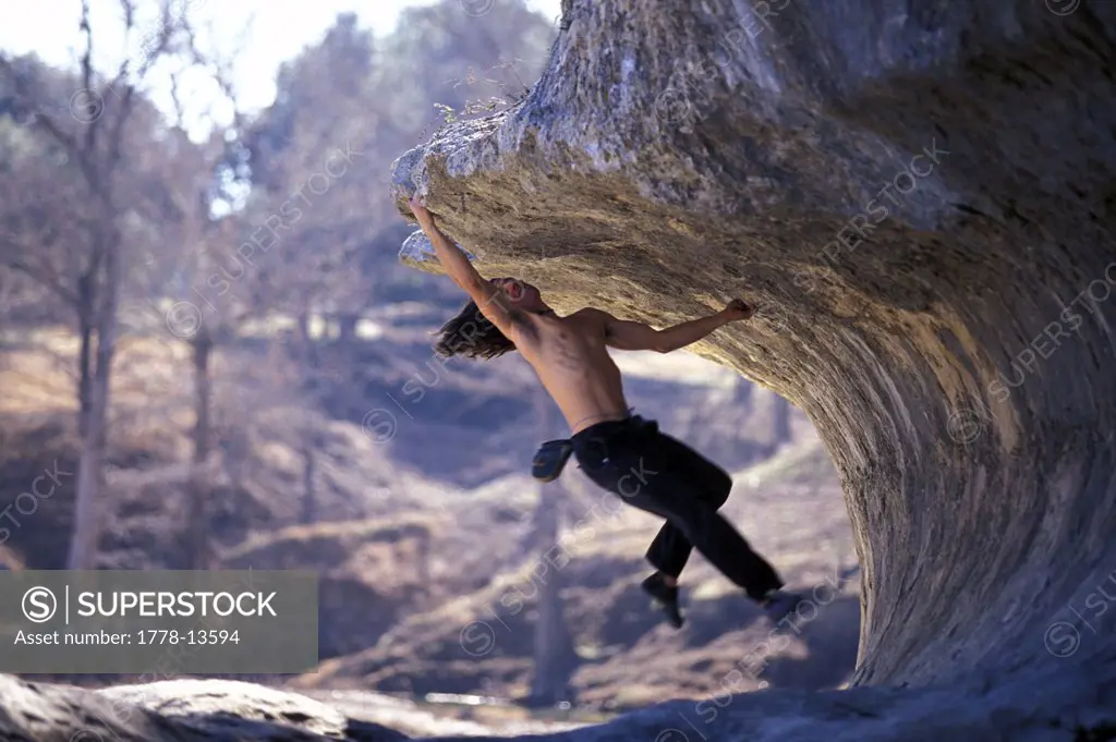 A shirtless climber bouldering on an overhang in the woods near Austin, Texas
