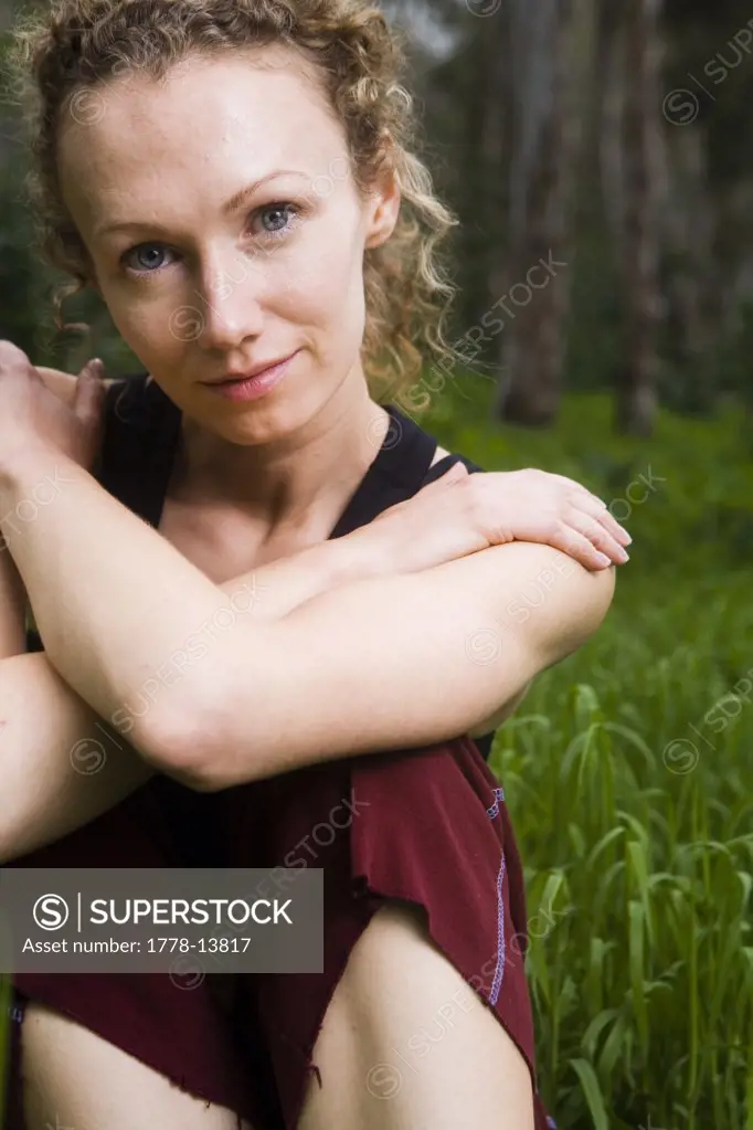 A blond-haired woman poses with hands together in a field of grass in front of trees in Carlsbad, California