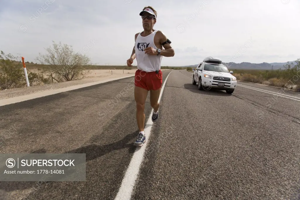 Man running on a highway with a support car during a marathon in Surprise, Arizona