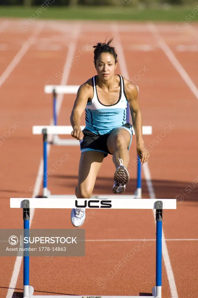 Attractive woman running hurdles on a track