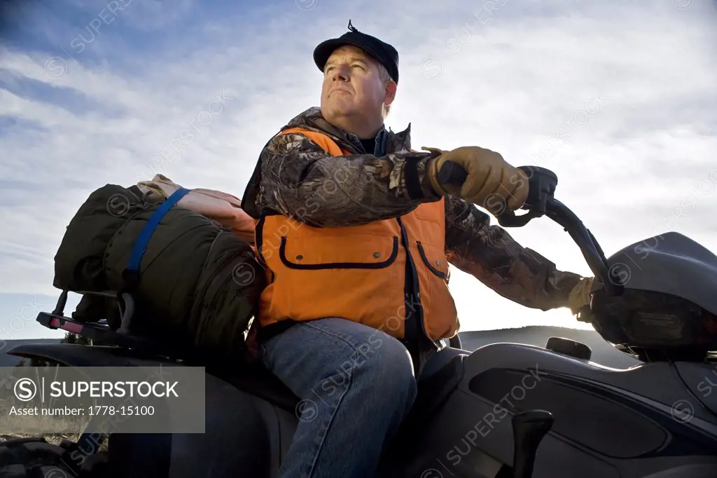 Male hunter with orange vest sitting on all terrain vehicle