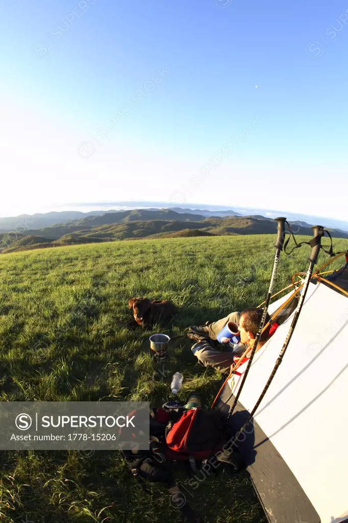 Male backpacker enjoys a cup of coffee with his chocolate labrador retriever at sunrise at a campsite along the Appalachian Trai