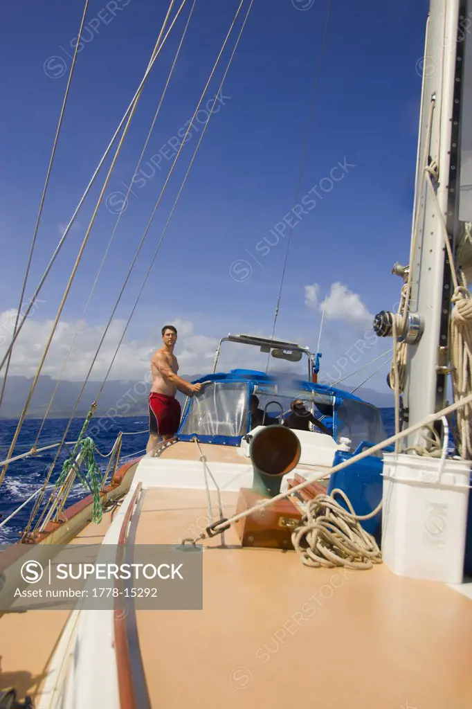 A man stands on the deck of a sailboat, Na Pali Coast, Kauai, Hawaii