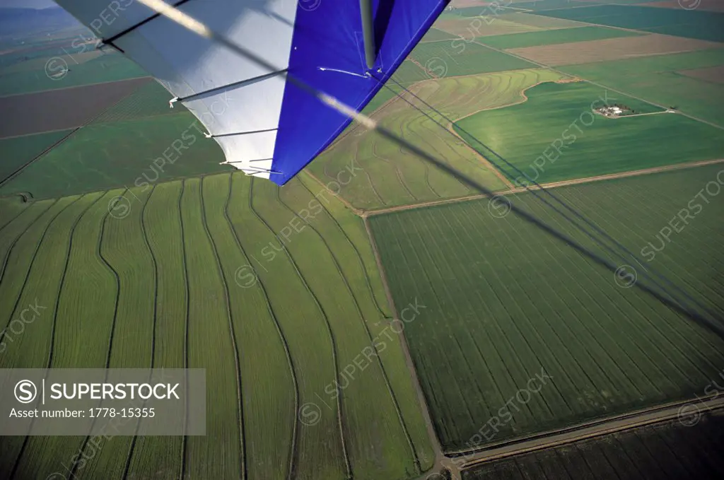 View from the wing of an ultralight plane over green fields