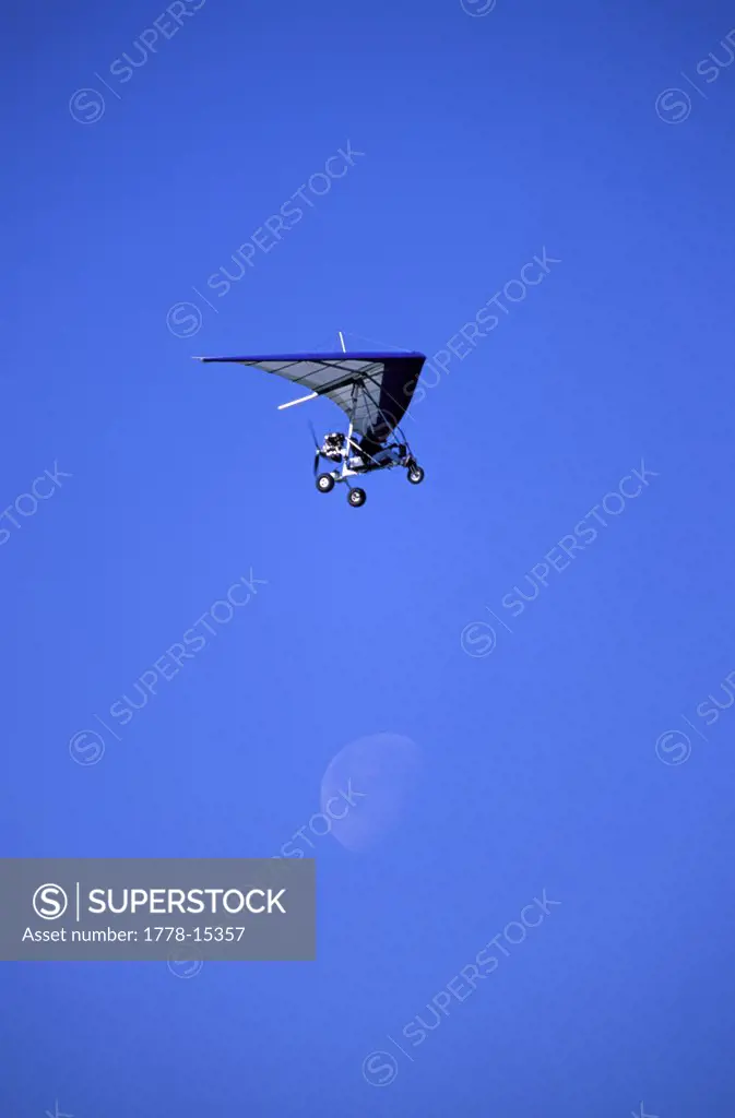 Ultralight plane flying over the moon in blue sky