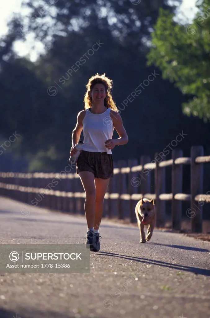 Woman and dog running by a fence (back lit)