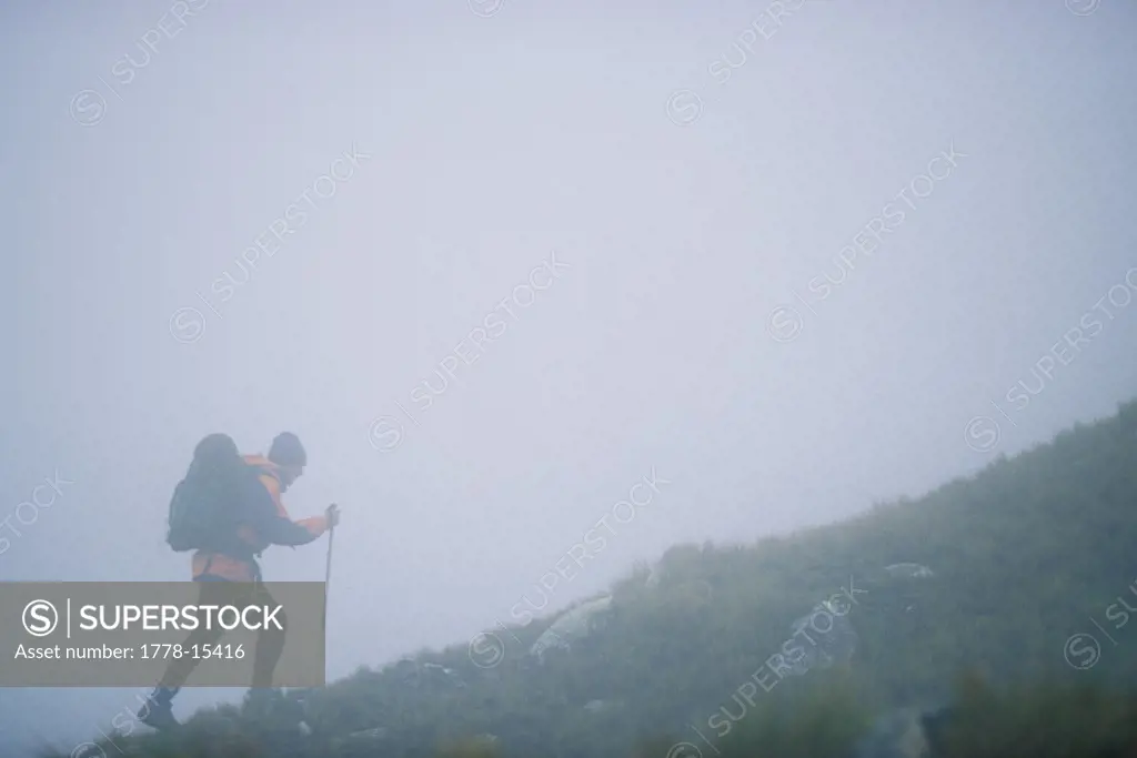 Man trekking-backpacking up a mountain in the fog