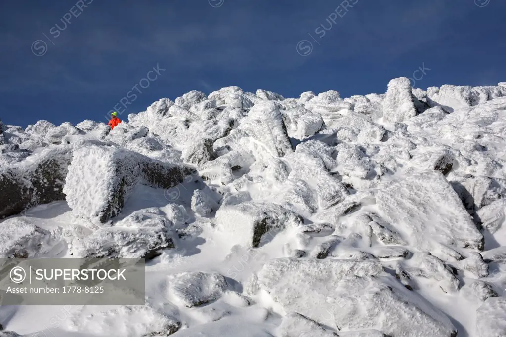 A lone hiker in bright clothing crosses the rocky terrain on Mt Washington in the White Mountains of New Hampshire