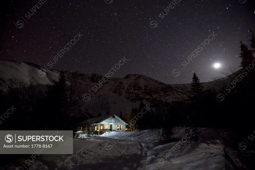 A moonlit trail outside a cabin shelter at night, with Tuckerman ravine in the background on Mt Washington in the White Mountains of New Hampshire