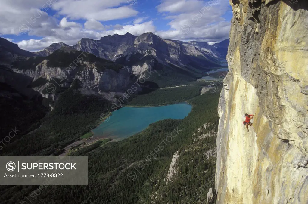 Male rock-climber scaling a big cliff with lakes in the background