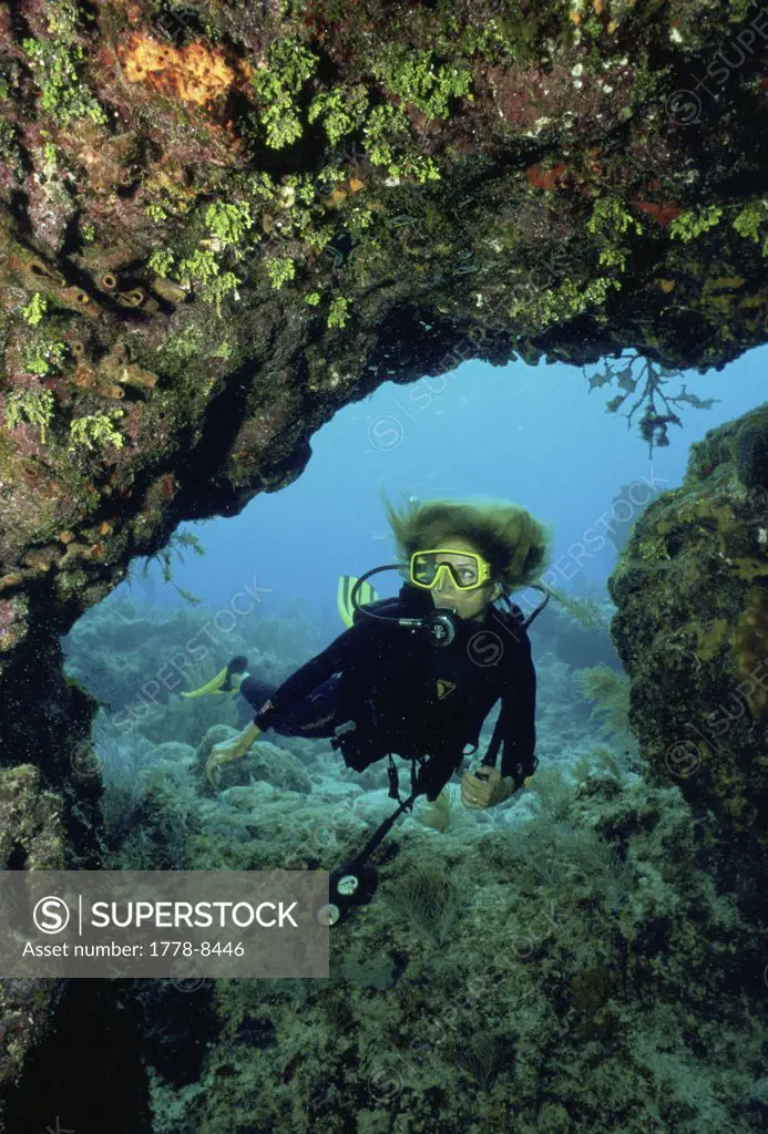 Female scuba diver swims through opening in coral, Key Largo