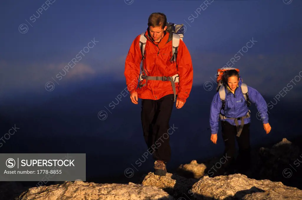 Man and woman hike up hill on a ridge