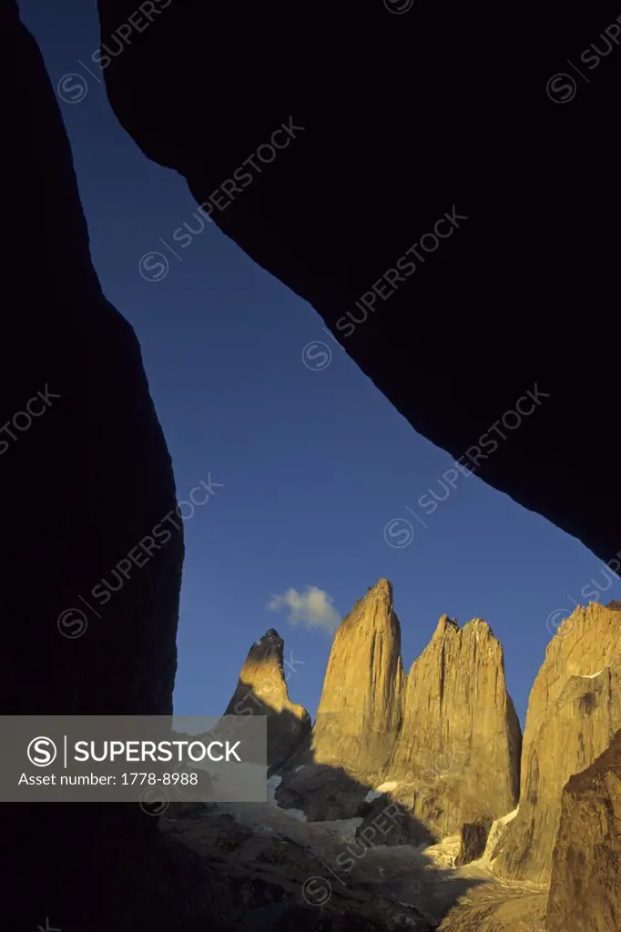 Three granite towers at sunrise viewed through a cleft of two silhouetted boulders, Torres Del Paine, Chile