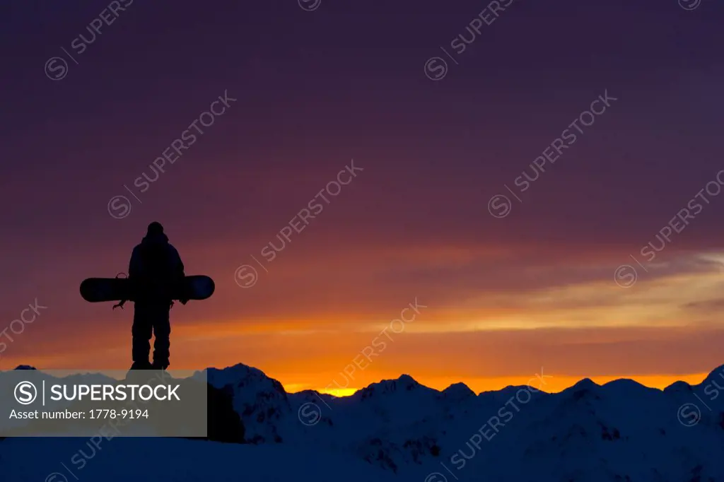 Snowboarder watches the sunset in the mountains