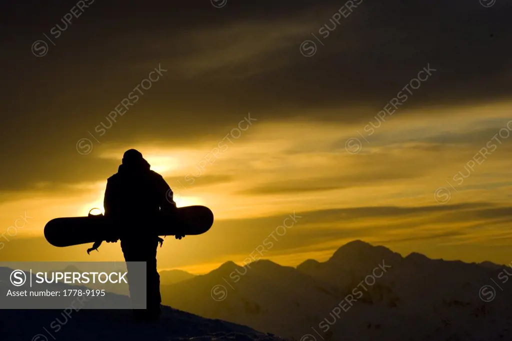 Snowboarder walks at sunset in the mountains
