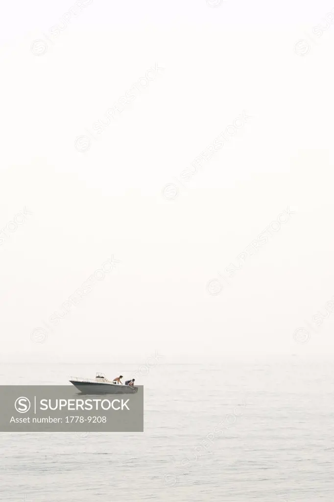Two youths getting ready to go for a swim off the back of a small powerboat on a hazy day
