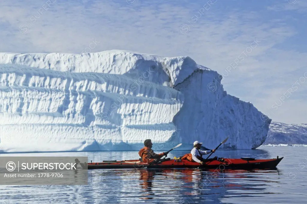 Sea kayakers paddling a tandem kayak pass an iceberg
