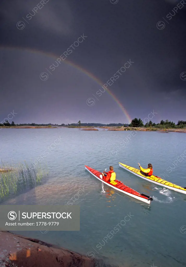 Young couple sea-kayak past rainbow on Georgian Bay, Lake Huron, Ontario, Canada