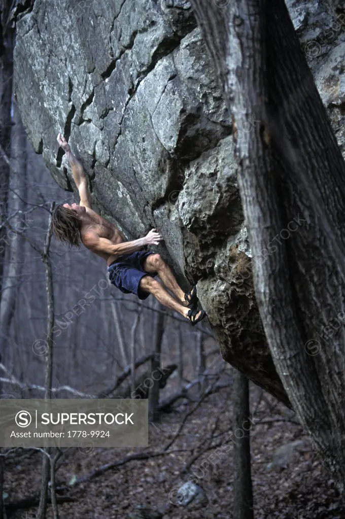 A man climbing on a steep sandstone boulder in the Ozark Mountains in Arkansas