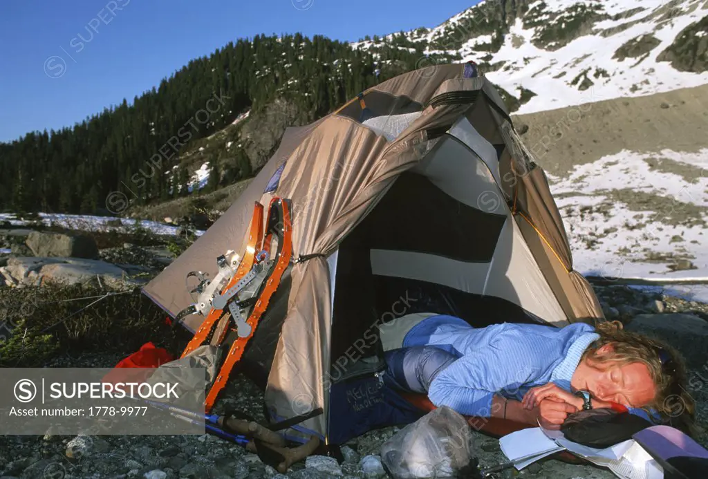 Woman sleeping in tent below snow covered mountain, British Columbia, Canada