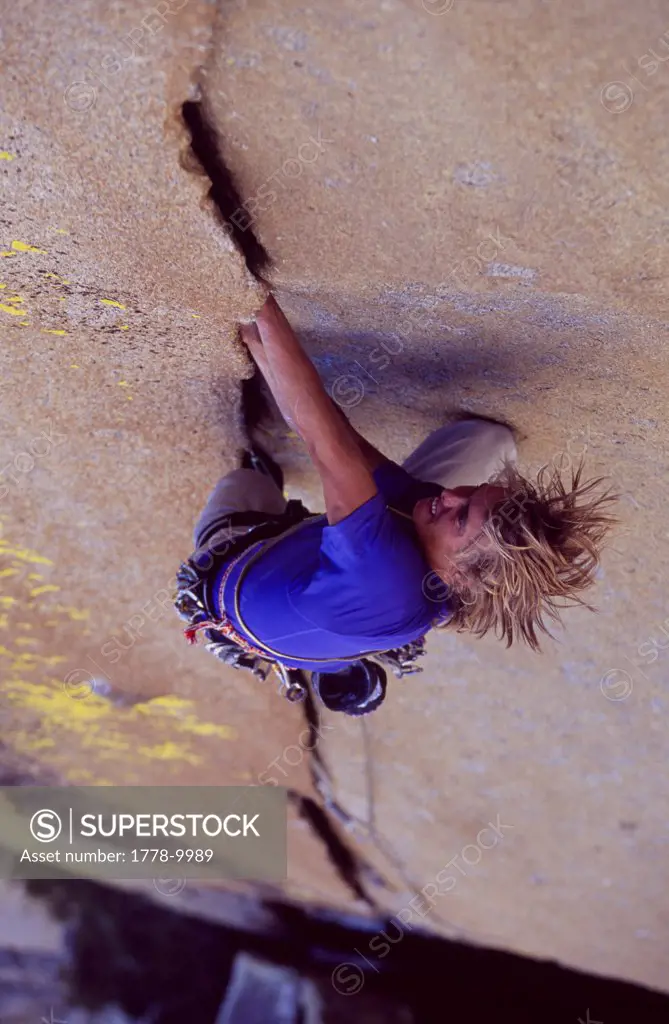 A man rock climbing a crack turns his head around quickly to look for a hold July 2005