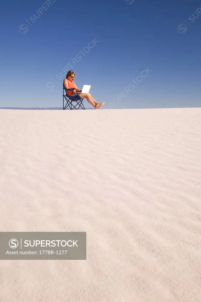 Woman using laptop in the sand dunes.