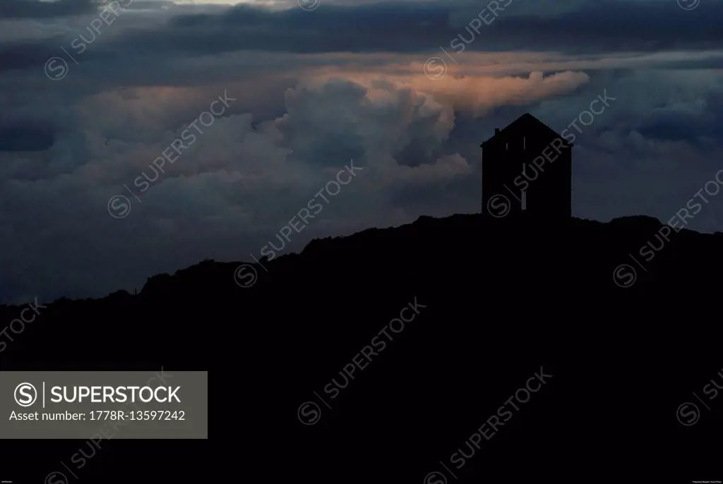 Mountain hut silhouette on stormy sky.