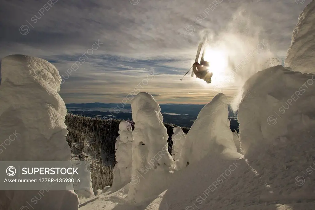 A skier throws a backflip off of a jump over snowcoated trees.