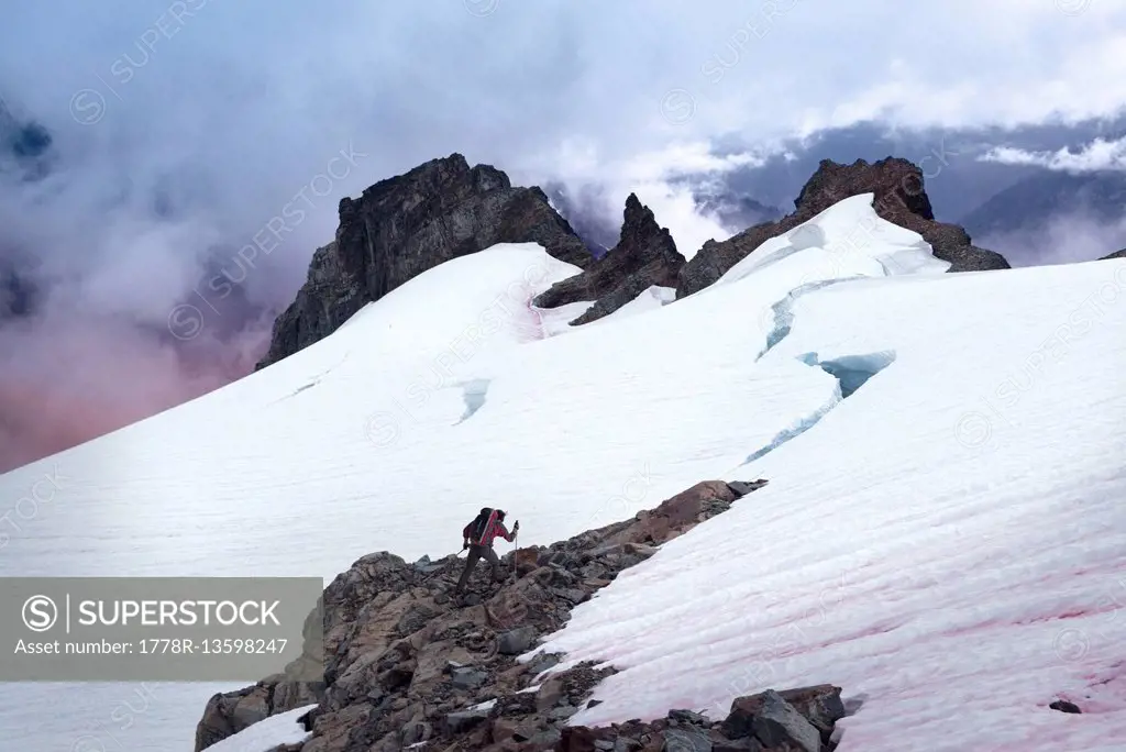 A mountaineer hikes toward a glacier crevasse during twilight.