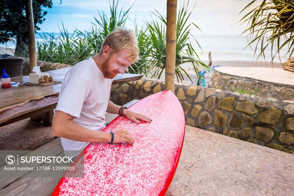 Surfer is waxing a board.