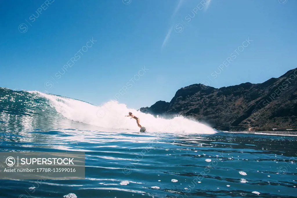 A girl surfs a wave in a bikini on a blue sky day