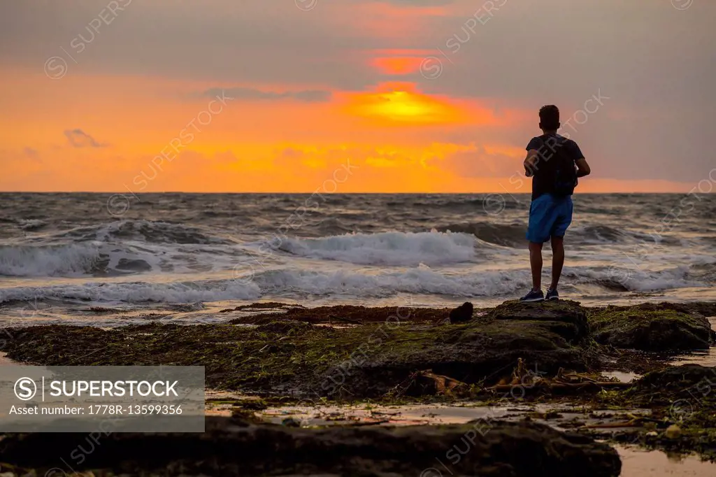 Man at ocean coastline at sunset.