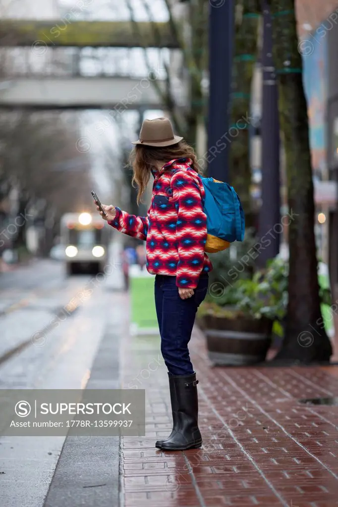 A woman with a cell phone standing by a street, waiting for a train in Portland, Oregon.
