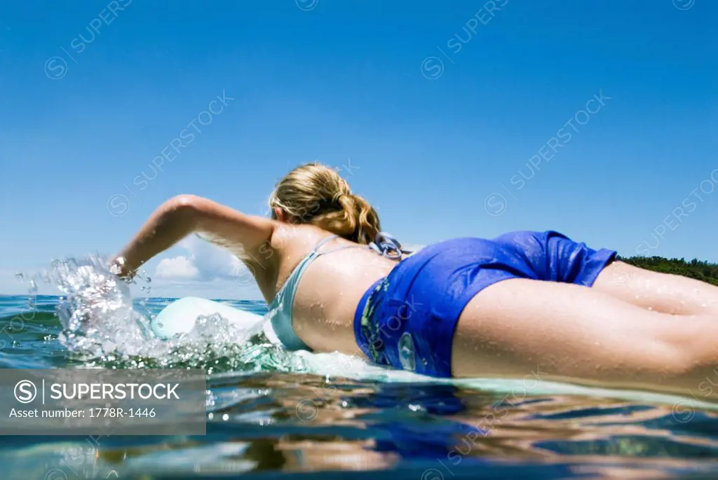 Woman paddling out on surfboard.