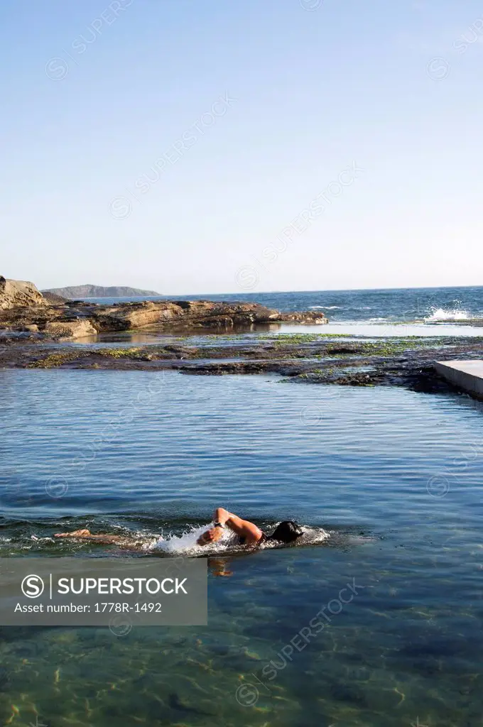 Man swims in ocean rock pool.