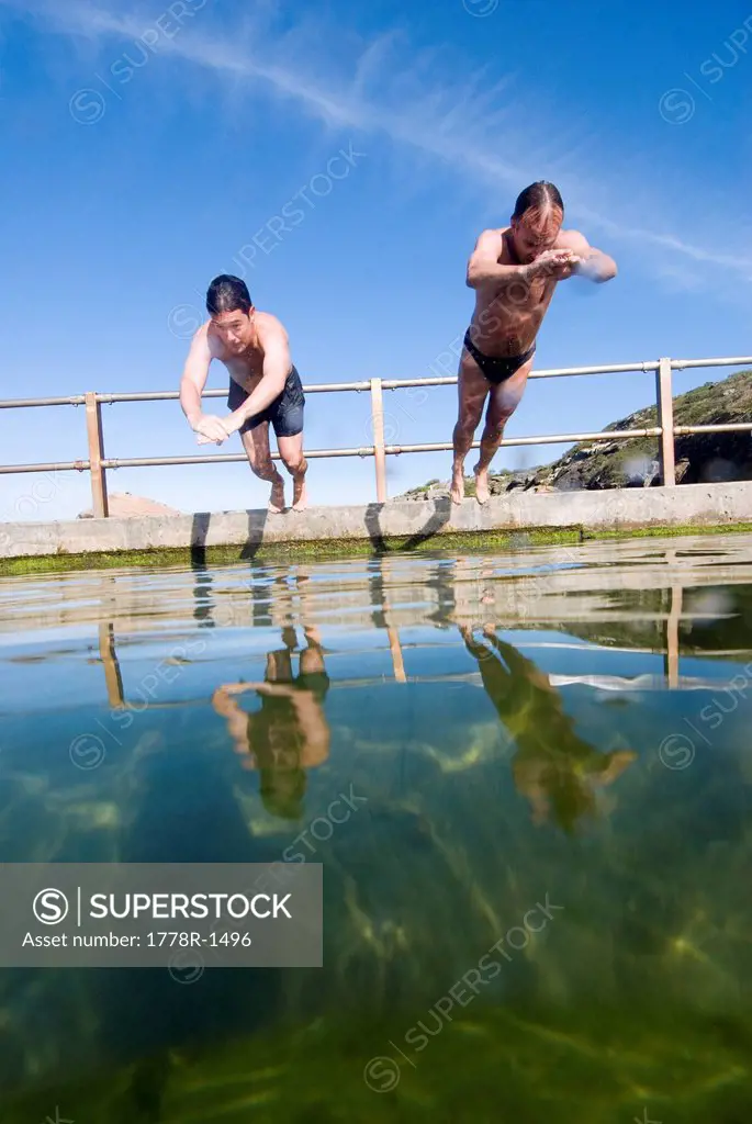 Men dive and swim in ocean rock pool.
