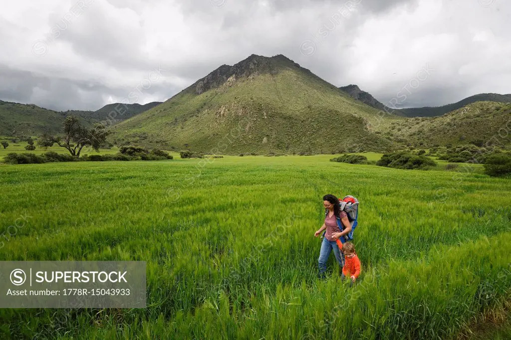 Mother with son hiking through field at archeological area of Xihuingo, Tepeapulco, Hidalgo, Mexico