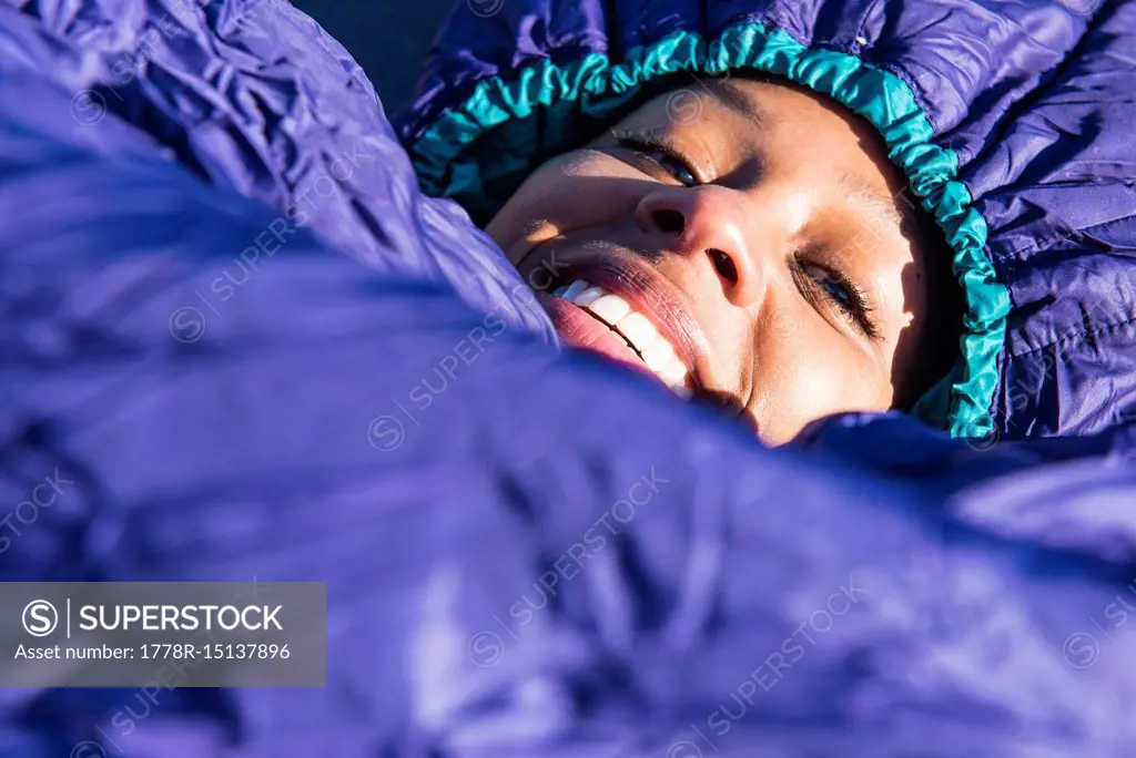 Portrait of young woman lying in purple sleeping bag and smiling at camera, Newburyport, Massachusetts, USA