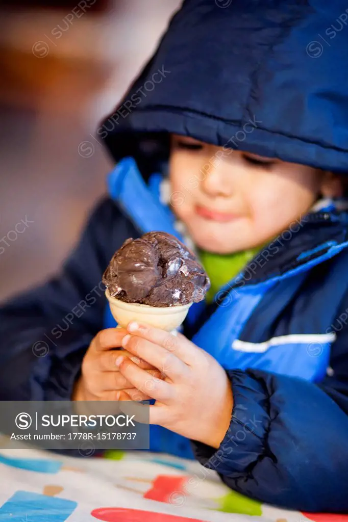 A 4 year old Japanese American boy holds an ice cream cone filled with chocolate ice cream.