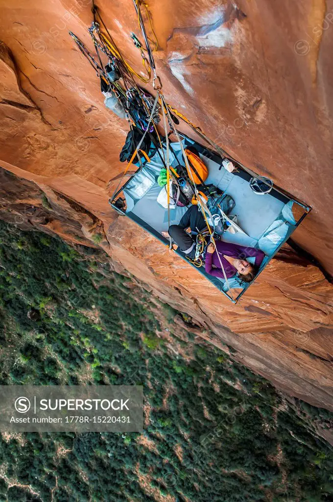 View from above of single young woman lying on portaledge while rock climbing Moonlight Buttress, Zion National Park, Utah, USA