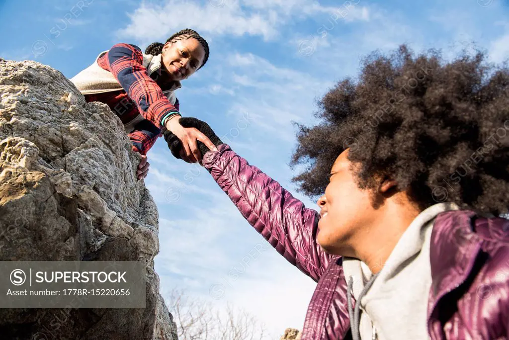 A young African American woman helping another woman up onto a rock on a sunny day