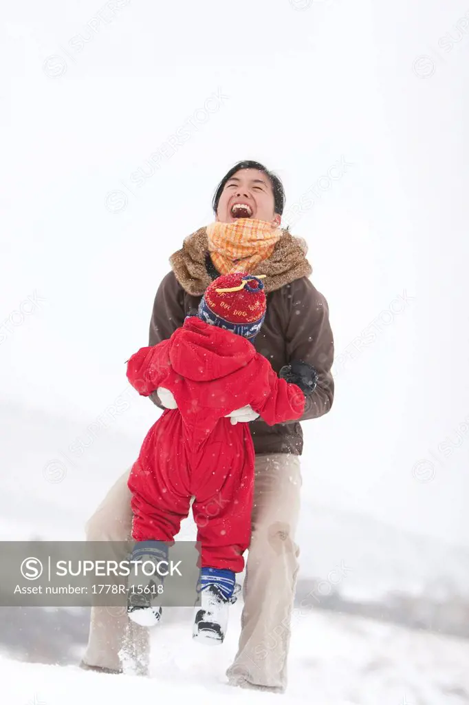 A two year old boy plays in a snowy field during a snowstorm in a red snowsuit with his mother in a park, Fort Collins, Colorado.