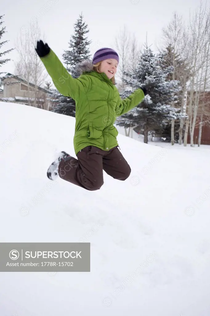 Young girl jumps into the snow and throw her hands up in the air.