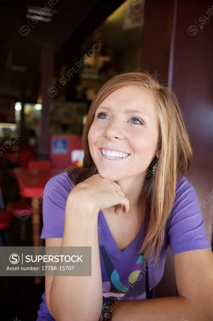 Young, woman sitting in a diner looks away and smiles.