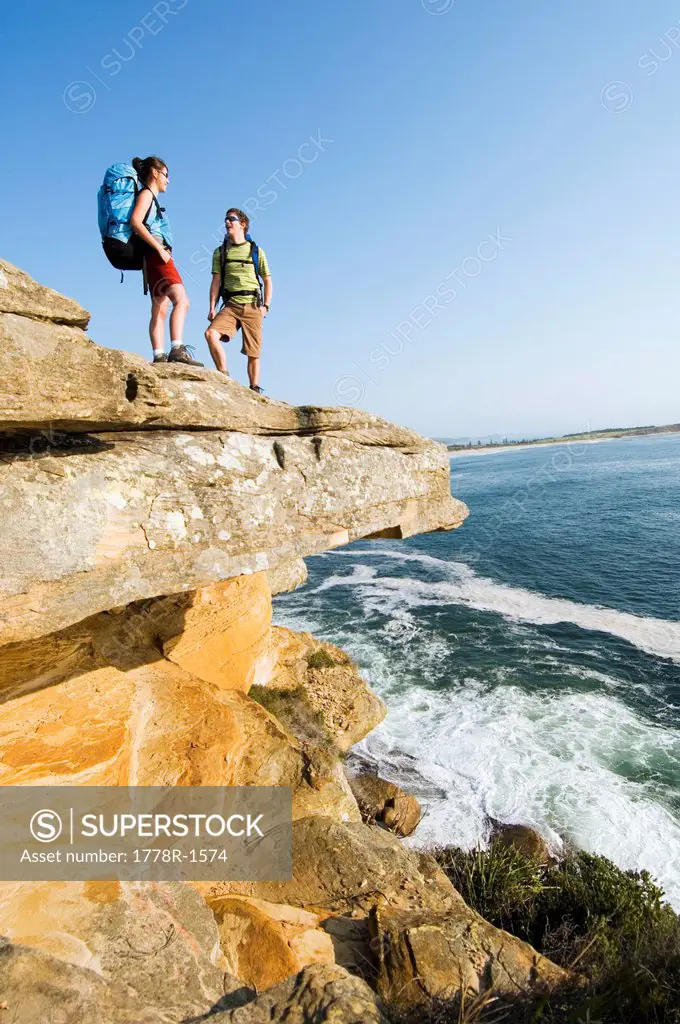 Hikers on edge of rocky ocean cliff.