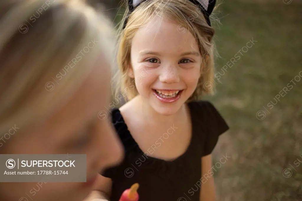 Girl holding her cold treat, wearing cat ears, looks at the camera and smiles.