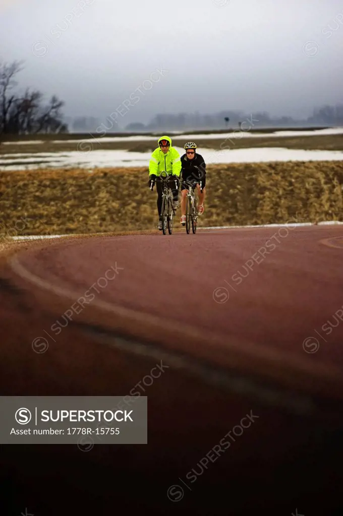 Two men bicycles on a cold and foggy winter day.